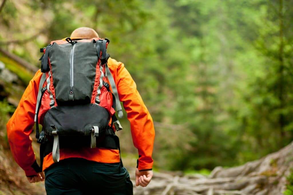 Young man in orange jacket walking hiking outdoors with backpack