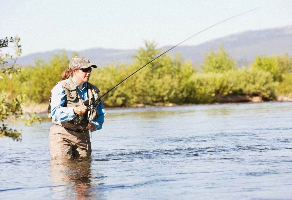 woman wearing waders is fly fishing