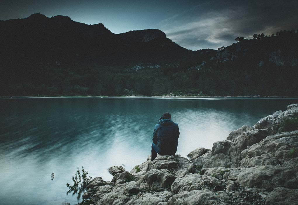 man standing along rocky shoreline for bass fishing