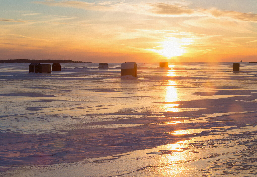 sunset on a lake with shelters for ice fishing