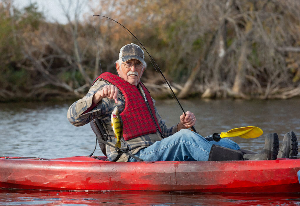 old man bass fishing from his kayak wearing a lifejacket